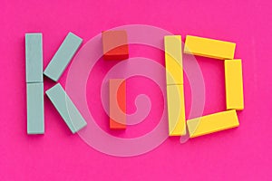 Word KID made from multicolored wooden bricks toys on purple paper background. Early childhood education and kids game