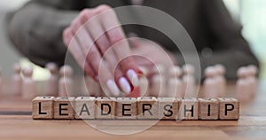 Word leadership and a hand placing red figurine and a group of identical wooden figurines