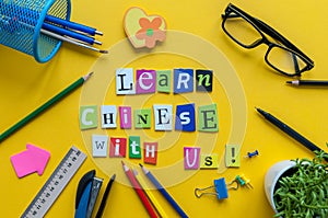 Word LEARN CHINESE WITH US made with carved letters on yellow desk with office or school supplies, stationery. Concept