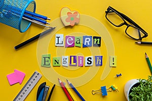 Word LEARN ENGLISH made with carved letters onyellow desk with office or school supplies, stationery. Concept of English