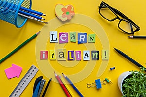 Word LEARN ITALIAN made with carved letters onyellow desk with office or school supplies, stationery. Concept of Italian