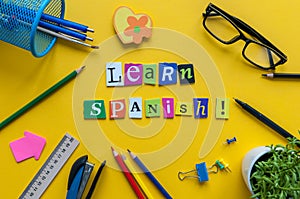 Word LEARN SPANISH made with carved letters on yellow desk with office or school supplies, stationery. Concept of