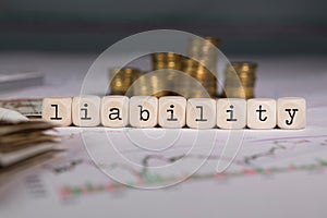 Word LIABILITY composed of wooden letter. Stacks of coins in the background