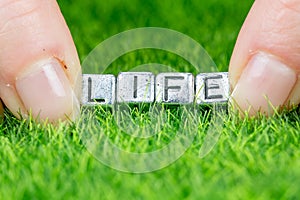 Word LIFE written in metal letters laid on grass and held between the fingers of a woman. Concept of wellness background