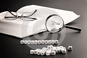 Word linguistics next to an open book, magnifying glass, pen and glasses. Concept of studying the humanities and linguistics. Dark