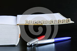 The word linguistics next to an open book and two pens. Black background. Concept for the study of liberal arts and linguistics at