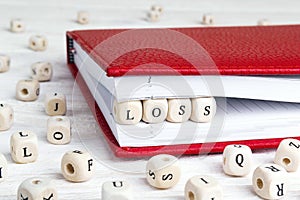 Word Loss written in wooden blocks in red notebook on white wood