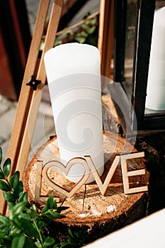 The word Love carved from wood, a white candle, standing on a wooden stump