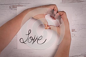 The word love painted on white paper with real human hands gesturing a heart shape with fingers