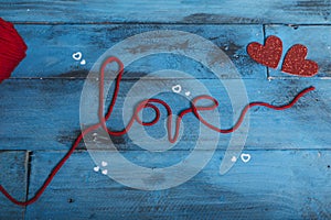 The word `love` with red wool threads and two hearts on blue wooden background. View from above Valentine`s day