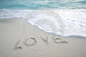 Word `Love` on the sandy beach with sea foam and sea wave.