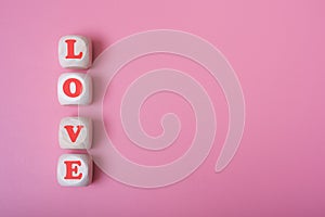 The word love is in the shape of a heart on wooden cubes on a pink background