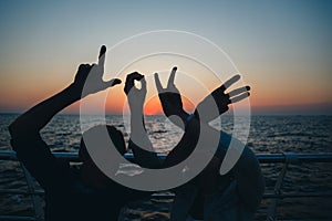 Word love silhouette of two young people making love shape of hands at the beach at sunrise sky summer time, seashore summer beach