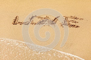 Word LOVE written in wet sand on the beach, sun shining over