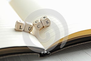 Word LUCK made with wooden cubes and open notebook on table, closeup