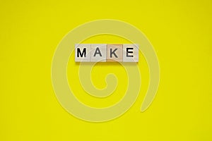 Word make. Top view of wooden blocks with letters on yellow surface