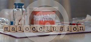 Word MALOCCLUSION composed of wooden dices. Pills, documents, pen, human jaw model in the background