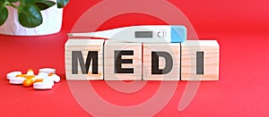 The word MEDI is made of wooden cubes on a red background. Medical concept