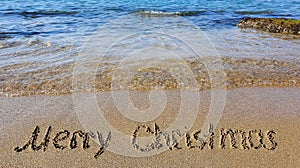 Word Merry Christmas written on the sand near the sea.