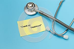 Word message `check up treatment` on yellow paper with stethoscope on blue background.