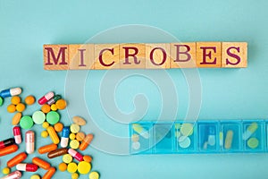 Word Microbes made with wooden cubes, many pills and box on light blue background, top view