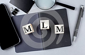 Word MLM on wooden block on black notebook with smartpone, credit card and magnifier