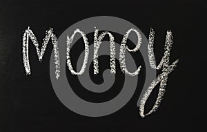 The word money written in white chalk on a black chalkboard