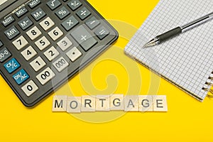 Word mortgage made with wood letters on yellow background and modern calculator with pen and notebook. Copy space. Economy, money