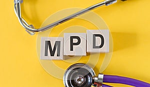 Word MPD - Multiple Personality Disorder, building from wooden cubes on yellow desk with stethoscope