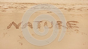 Word NATURE hand written in wet sand of beach