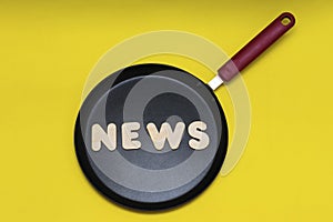 Word news made of wooden letters on a frying pan, yellow background. News preparation concept. The photo