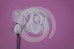 Word NO hand written on a heap of white sugar with full teaspoon of sugar on a pink background top view.