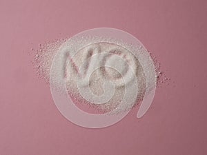 Word NO hand written on a heap of white sugar on a pink background top view.
