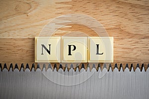 Word NPL Non Pperforming Loan on saw blade with wooden table background macro shot. Personal loan financial, risk management