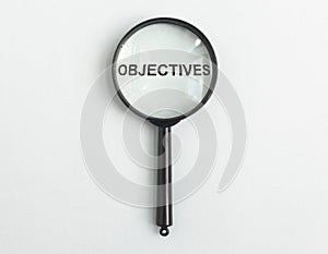 Word objectives through magnifying glass on light blue gary background. Target concept