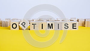 the word optimise is made of wooden cubes lying on a yellow table. one of the cubes is placed on an edge, concept