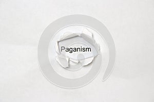 Word Paganism on white isolated background through the wound hole in the paper. photo