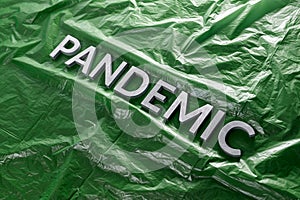 The word pandemic laid with silver letters on crumpled green plastic film - diagonal perspective composition with selective focus