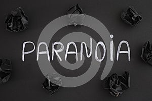The word Paranoia on a black background with black crumpled paper balls around it photo