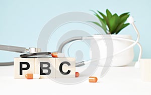The word pbc is written on wooden cubes near a stethoscope on a wooden background. Medical concept
