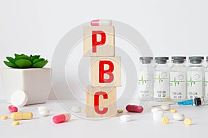 The word pbc is written on wooden cubes near a stethoscope on a wooden background. Medical concept
