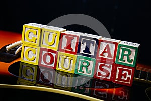 Word or phrase Guitar Course made with letter cubes, standing on guitar.