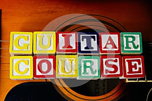 Word or phrase Guitar Course made with letter cubes, standing on guitar.