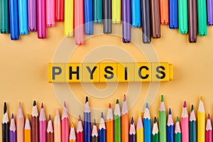 Word physics written on yellow cubes in frame from colorful school supplies.