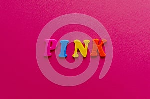 Word `pink` from plastic colored magnet letters on pink paper ba