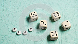 The word `Play` is composed of multicolored wooden letters and game dice on a mint background.