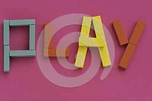 Word PLAY made from multicolored wooden bricks toys on purple paper background. Kids game concept. Bright colors of red