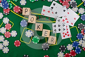 The word poker on wooden cubes, poker chips with playing cards on the green casino table