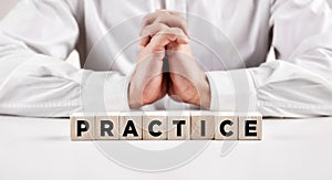 The word practice written on wooden cubes with a businessman with crossed hands at the background. Practice makes perfect