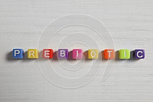 Word Prebiotic made of colorful cubes on wooden table, flat lay